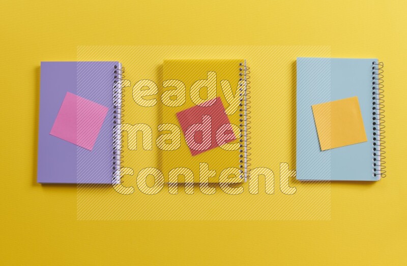 Multicolored notebooks with school supplies on yellow background