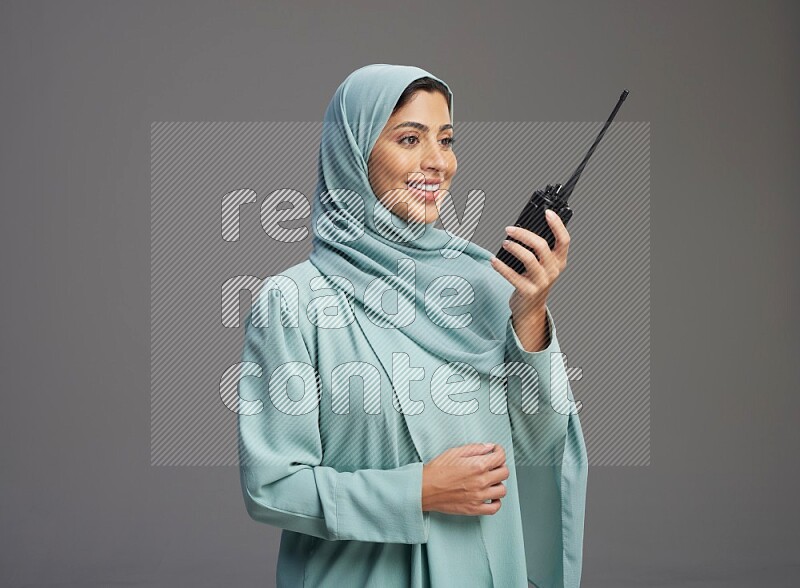 Saudi Woman wearing Abaya standing holding walkie-talkie on Gray background