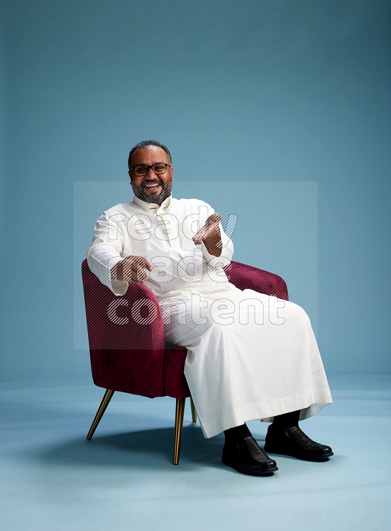 Saudi Man without shimag sitting on chair holding ATM card on blue background