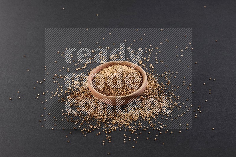 A wooden bowl full of mustard seeds and more seeds spread on a black flooring in different angles