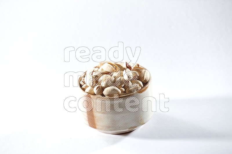 A beige ceramic bowl full of pistachios on a white background in different angles