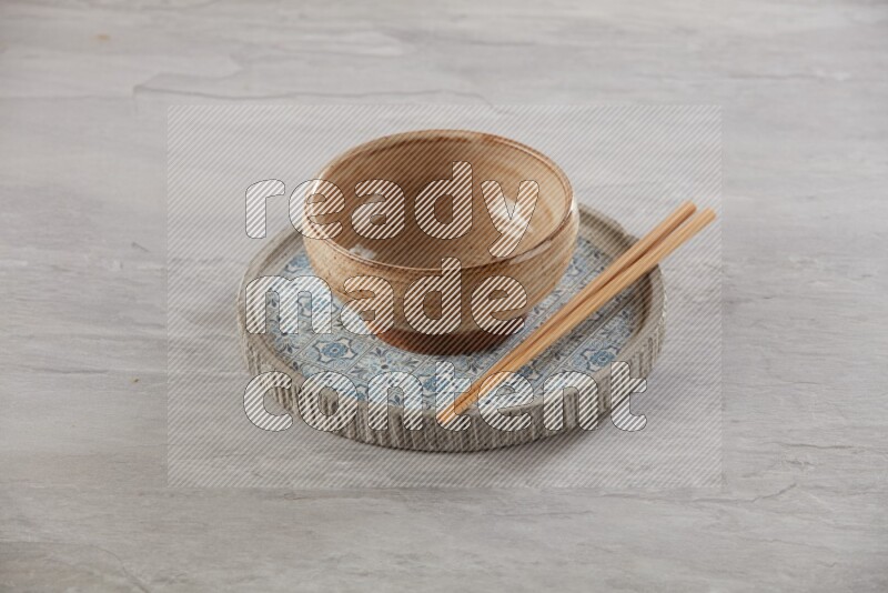 multi color pottery round bowl on top of multi color round ceramic plate and chopsticks, on grey textured countertop