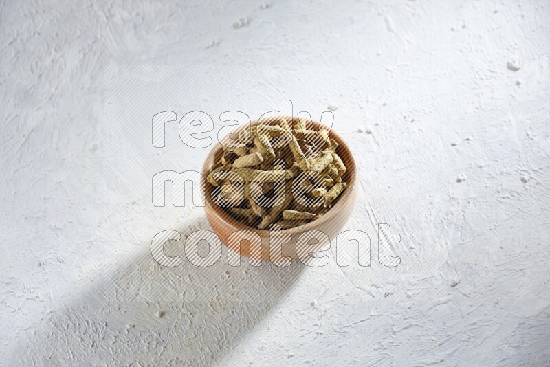 A wooden bowl full of dried turmeric whole fingers on a textured white flooring