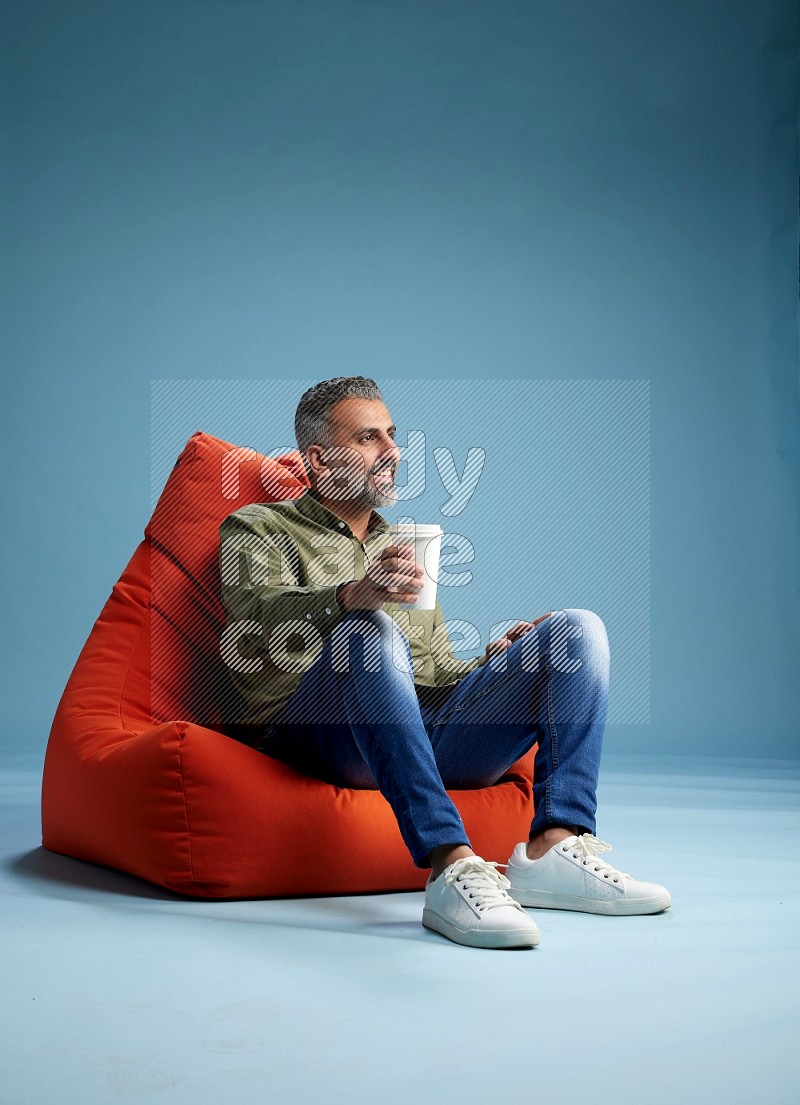 A man sitting on an orange beanbag and drinking coffee