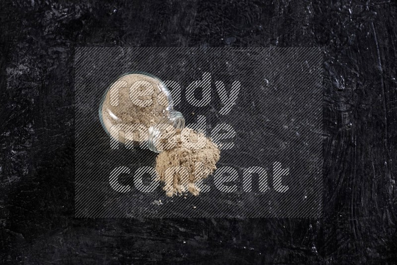 A glass spice jar full of garlic powder flipped and the powder came out on a textured black flooring in different angles