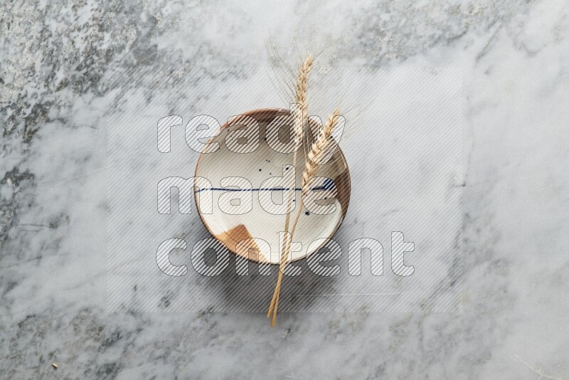 Wheat stalks on multicolored pottery plate on grey marble background
