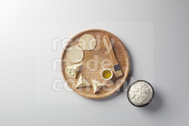 two closed sambosas and one open sambosa filled with cheese while flour, and oil with oil brush aside in a wooden dish on a white background