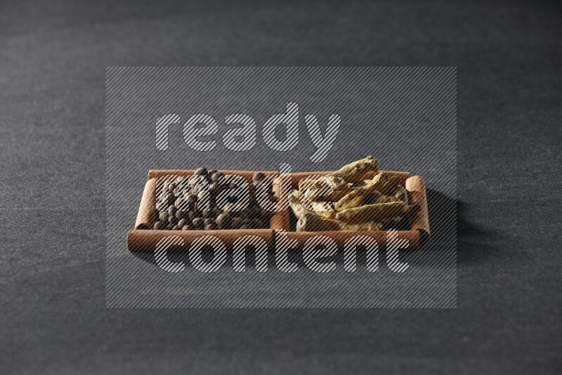 مربعان من أعواد القرفة ممتلئان ببهار الفلفل الحلو وأصابع الكركم علي خلفية سوداء