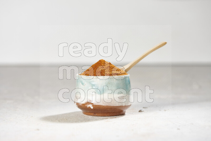 A colored pottery bowl full of ground paprika powder on white background