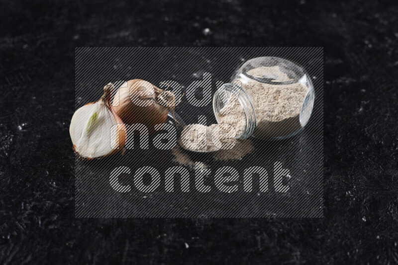 A glass jar full of onion powder flipped with some spilling powder on black background