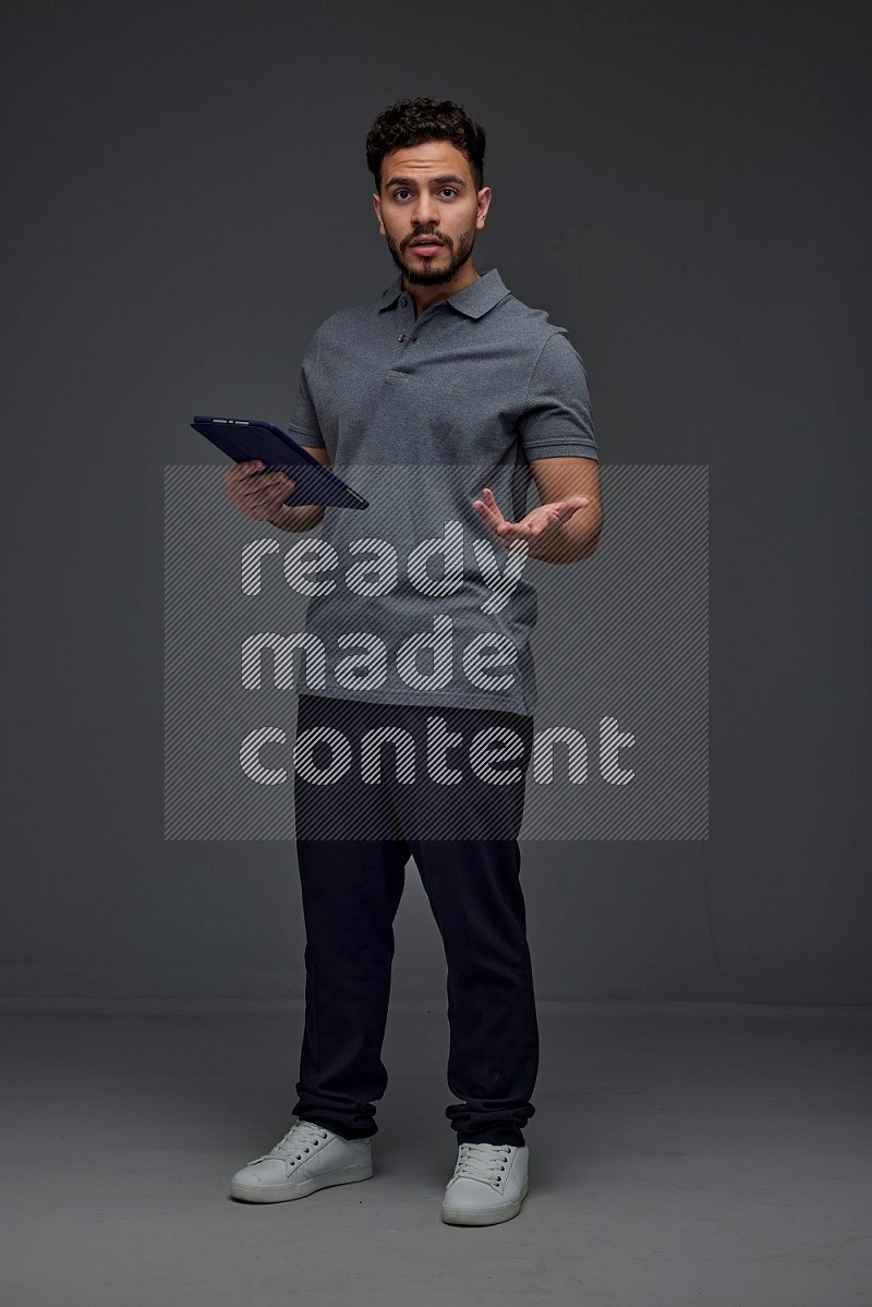 A man wearing casual standing and using his tablet and making multi hand gestures different angles eye level on a gray background