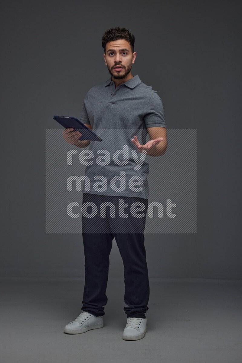 A man wearing casual standing and using his tablet and making multi hand gestures different angles eye level on a gray background