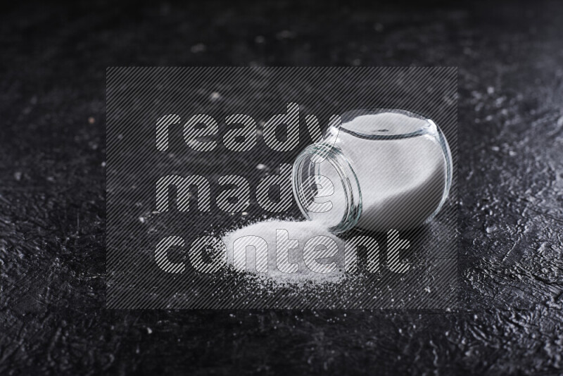 A glass jar full of fine table salt on black background