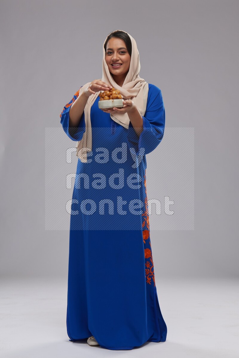 A Saudi woman standing wearing Jalabeya holding a plate of luqaimat