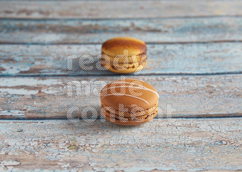 45º Shot of of two assorted Brown Irish Cream, and Yellow Crème Brulée macarons on light blue background