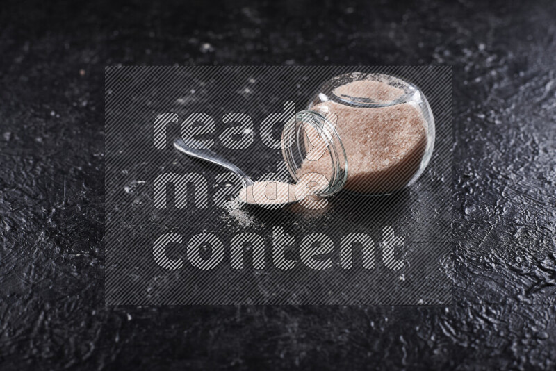 A glass jar full of fine himalayan salt on black background