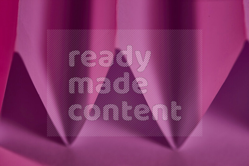 A close-up abstract image showing sharp geometric paper folds in pink gradients