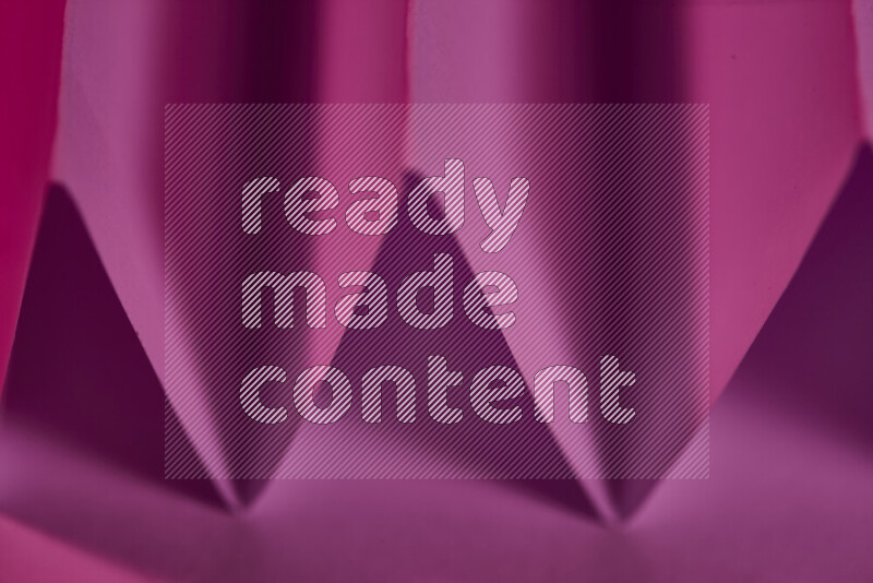 A close-up abstract image showing sharp geometric paper folds in pink gradients