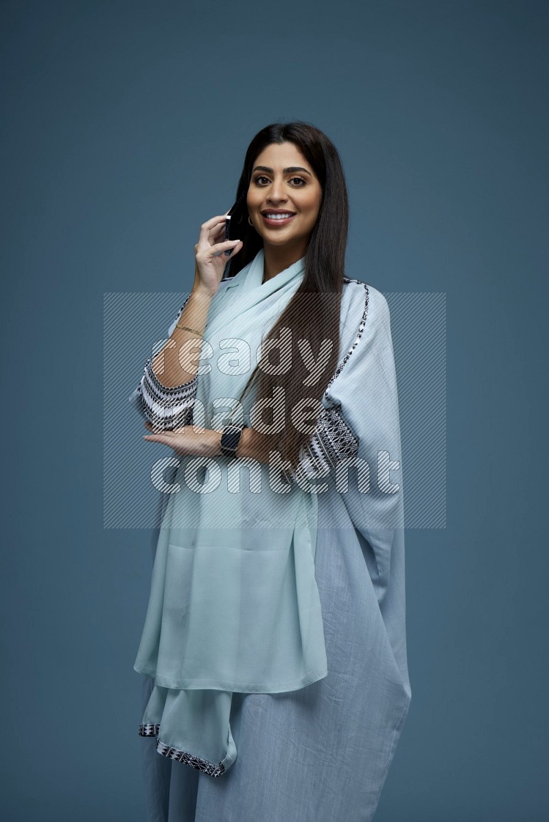 A Saudi woman having a Call in a blue background wearing a blue Abaya with no hijab