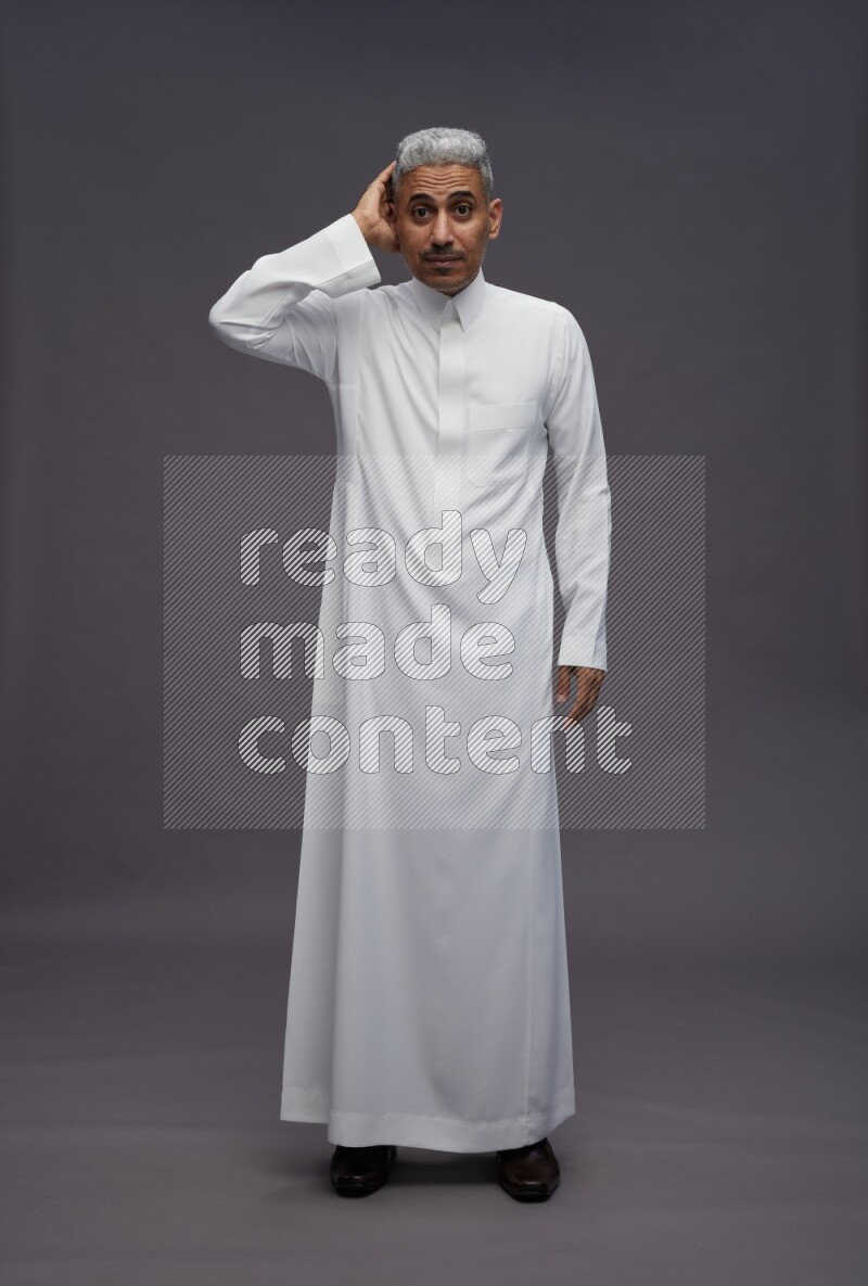 Saudi man wearing thob standing interacting with the camera on gray background