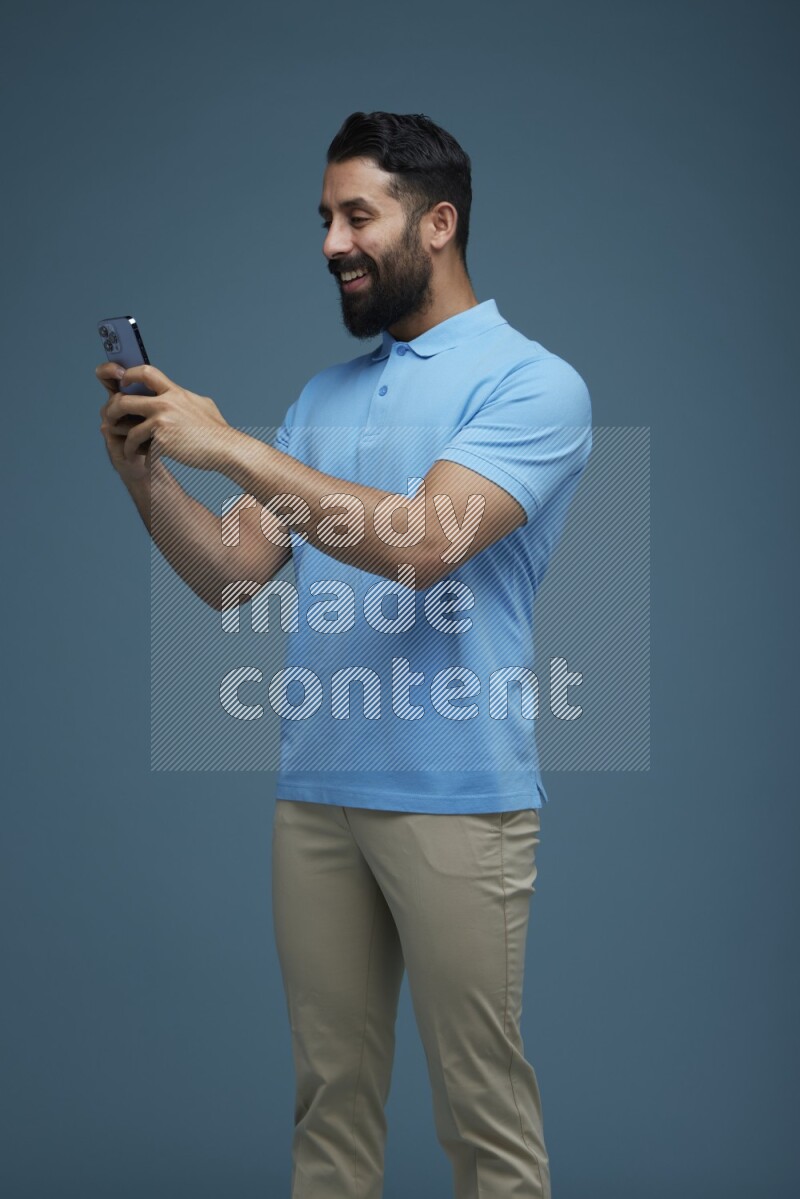 A man Texting on his phone in a blue background wearing a Blue shirt