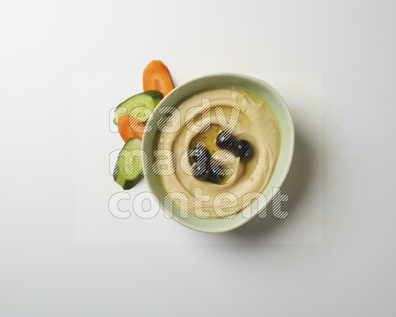 Hummus in a green plate garnished with black olives on a white background