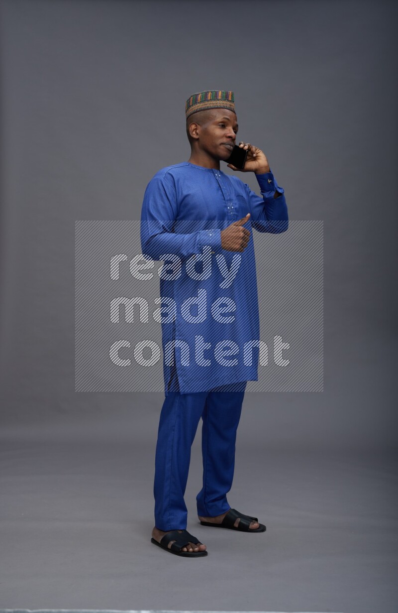 Man wearing Nigerian outfit standing talking on phone on gray background