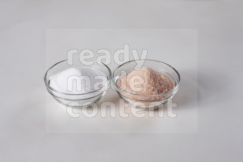 2 glass bowls one is filled with himalayan salt and the other with white salt on white background