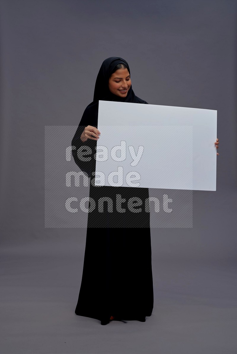 Saudi woman wearing Abaya standing holding white board on gray background