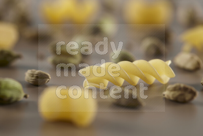 Raw pasta with different ingredients such as cherry tomatoes, garlic, onions, red chilis, black pepper, white pepper, bay laurel leaves, rosemary and cardamom on beige background