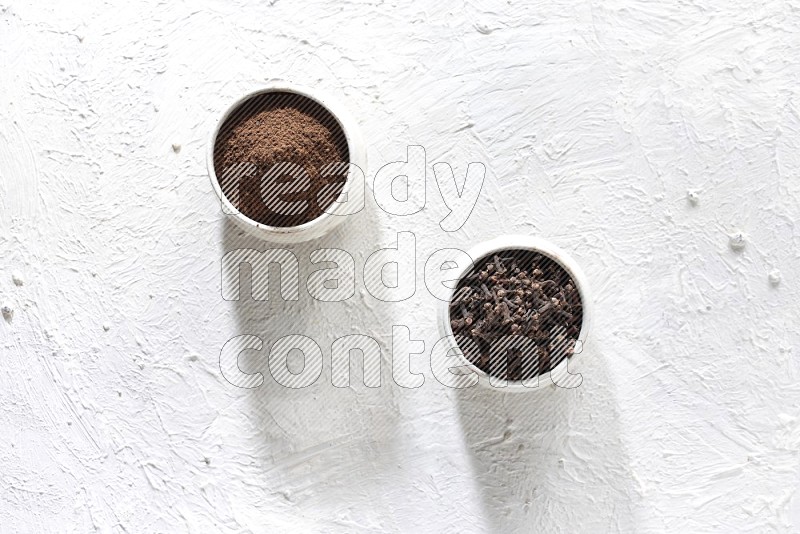 2 Beige ceramic bowls, one full of cloves and the other full of powder on textured white flooring