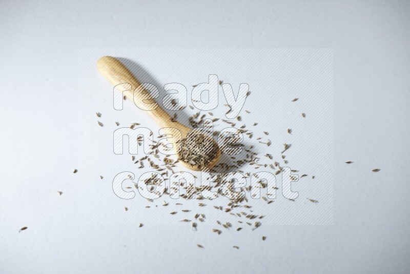 A wooden spoon full of cumin seeds on a white flooring