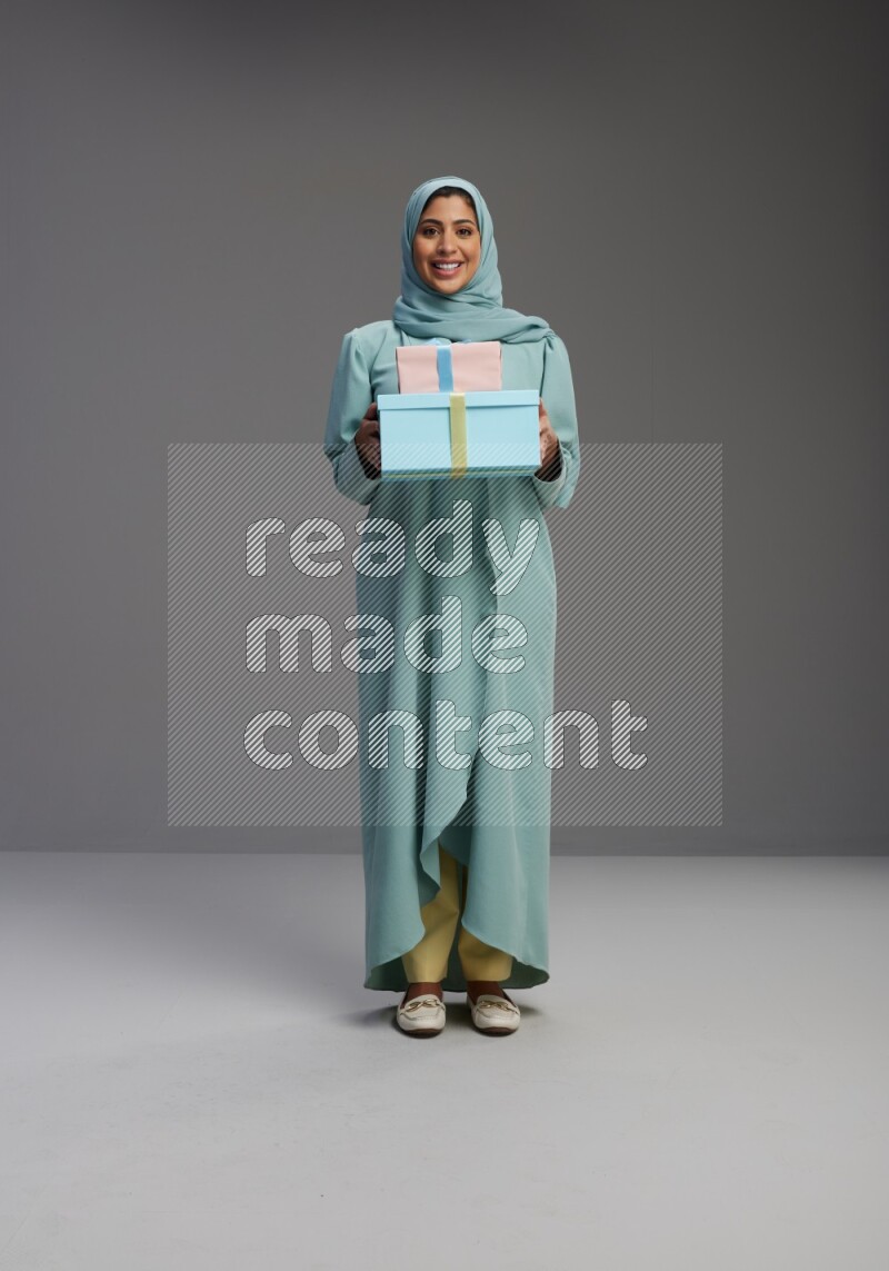 Saudi Woman wearing Abaya standing holding gift box on Gray background