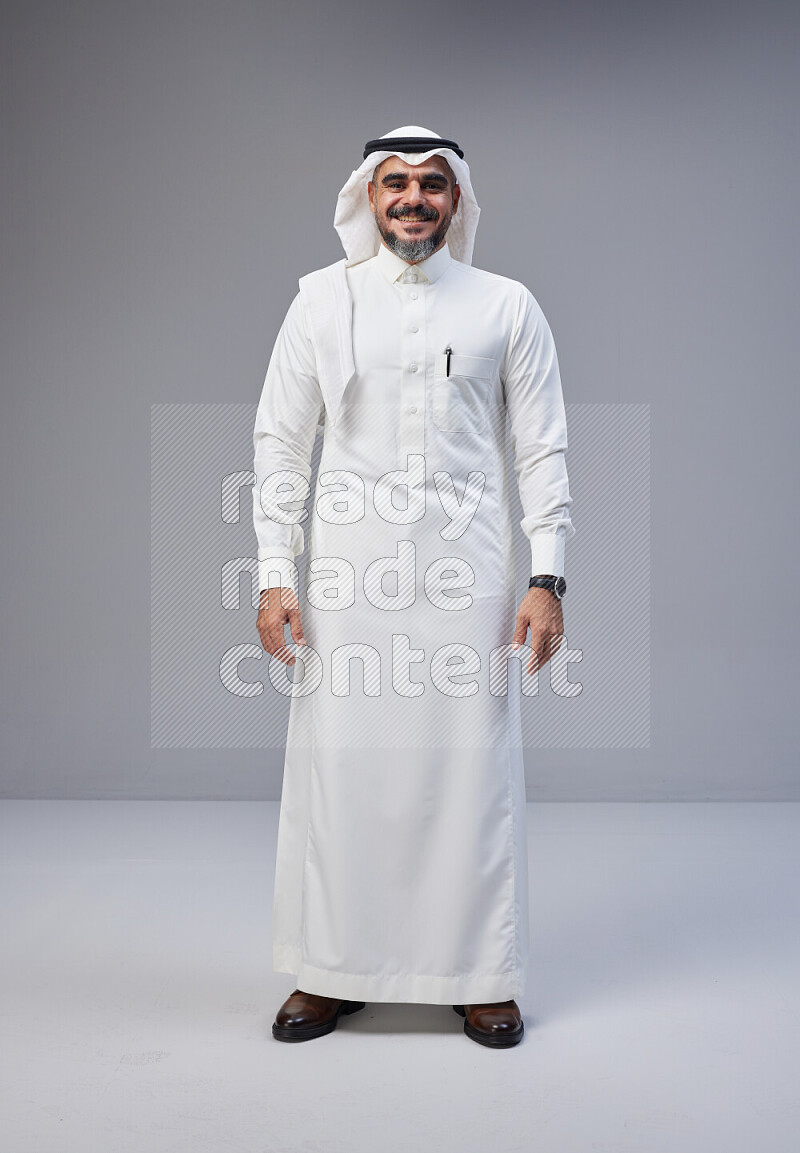 Saudi man Wearing Thob and white Shomag standing interacting with the camera on Gray background