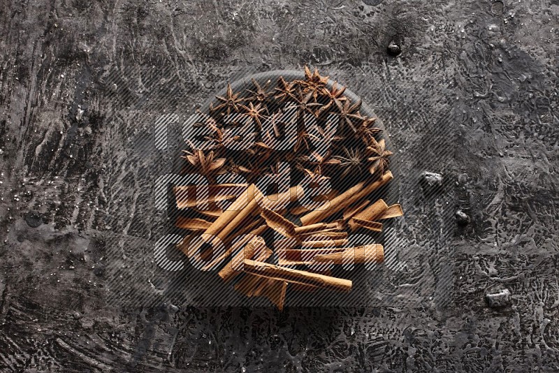 Cinnamon sticks and star anise on a black plate on textured black background