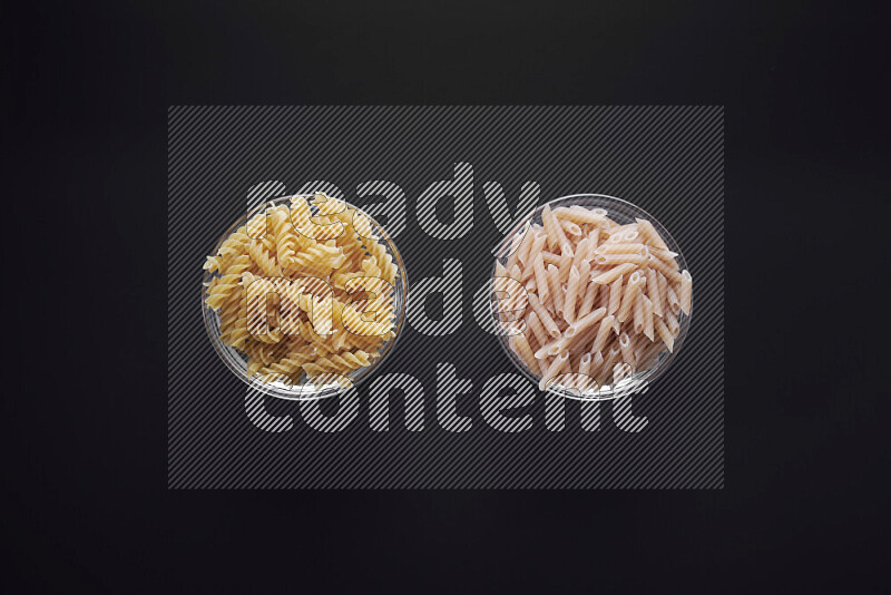 Different pasta types in glass bowls on black background