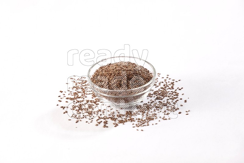 A glass bowl full of flax seeds surrounded by flax seeds on a white flooring