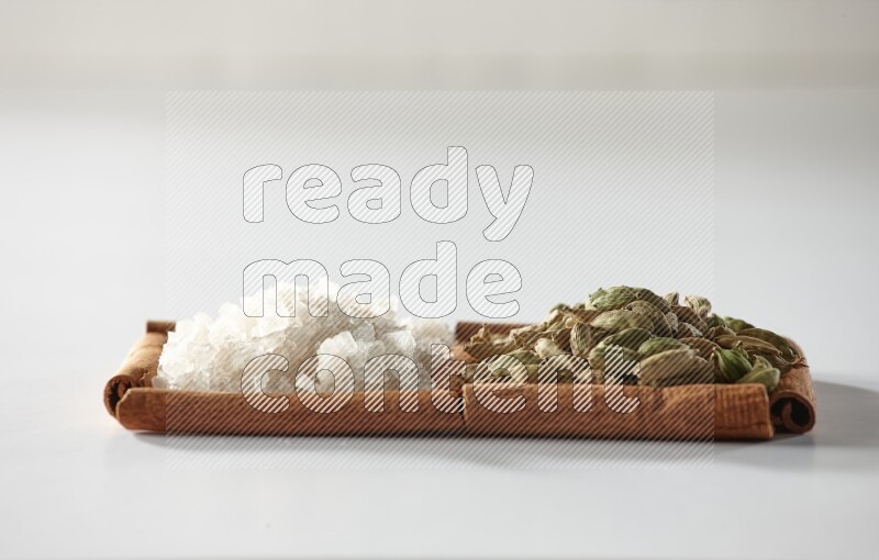 مربعان من أعواد القرفة ممتلئان بحبوب الهيل والملح الأبيض علي خلفية بيضاء