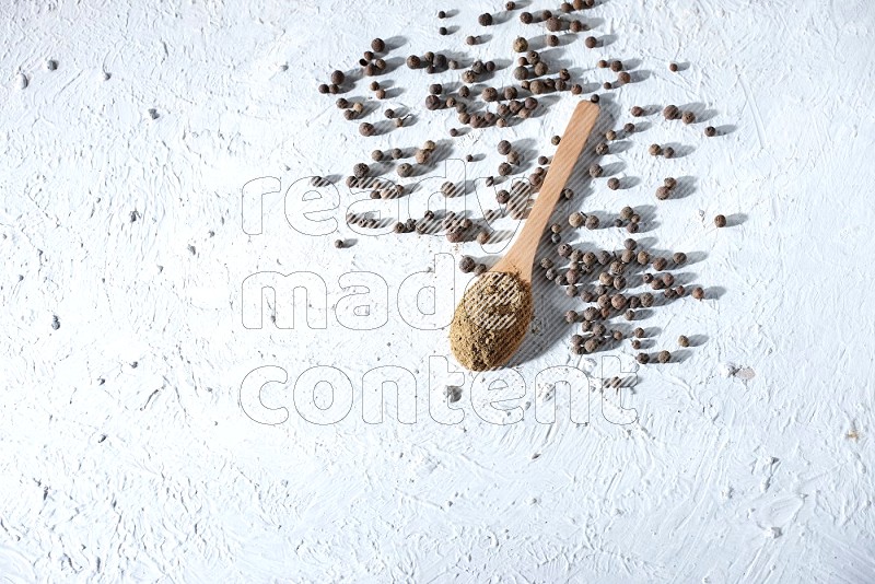 Wooden spoons full of allspice powder and allspice whole balls spreaded on a textured white flooring