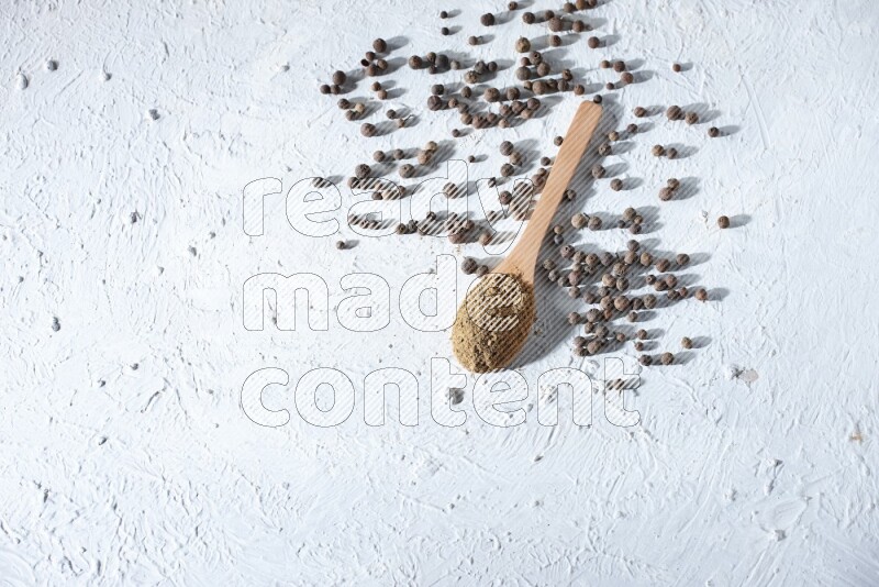 Wooden spoons full of allspice powder and allspice whole balls spreaded on a textured white flooring