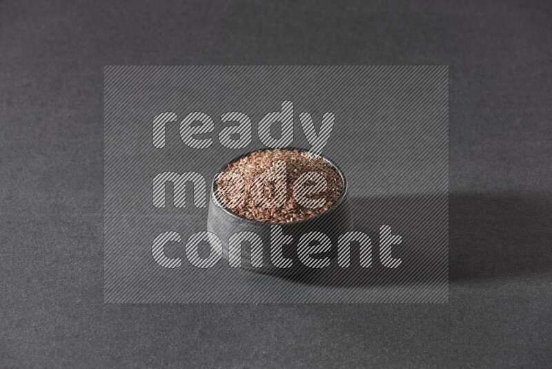 A black pottery bowl full of flaxseeds on a black flooring