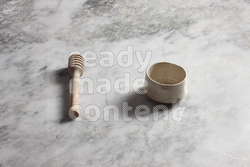 Beige pottery bowl with wooden honey dipper on the side on grey marble background