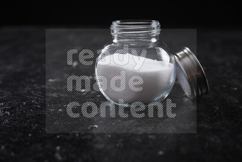 A glass jar full of fine table salt on black background