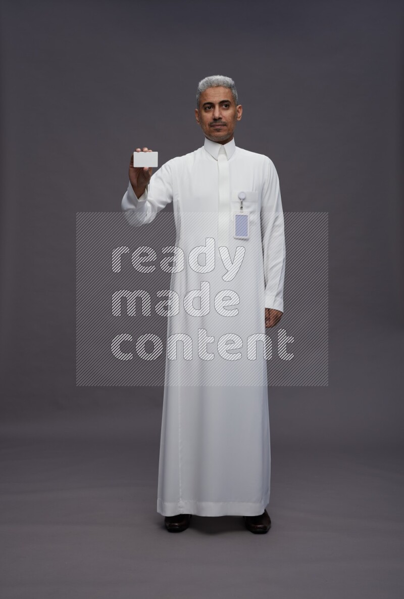 Saudi man wearing thob with pocket employee badge standing holding ATM card on gray background