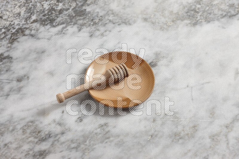 Multicolored pottery plate with wooden honey dipper in it on grey marble background