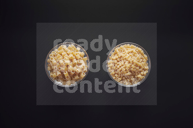 Different pasta types in glass bowls on black background