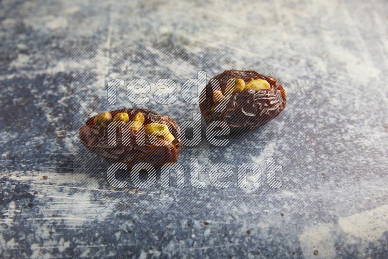 two pistachios stuffed madjoul dates on a rustic blue background