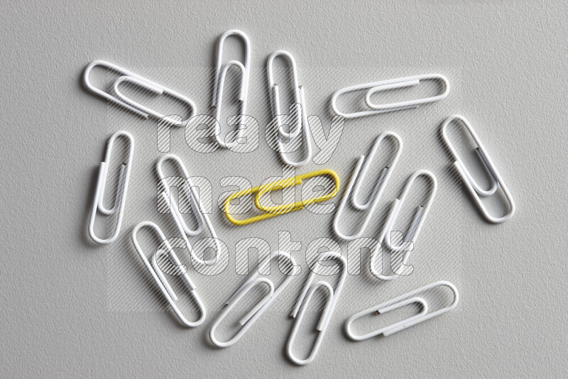 A yellow paperclip surrounded by bunch of white paperclips on grey background