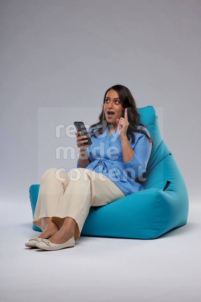 A woman sitting on a blue beanbag and texting on phone