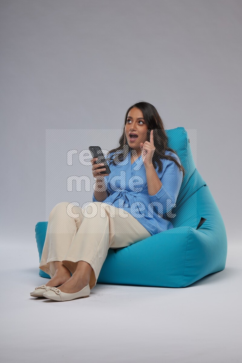 A woman sitting on a blue beanbag and texting on phone